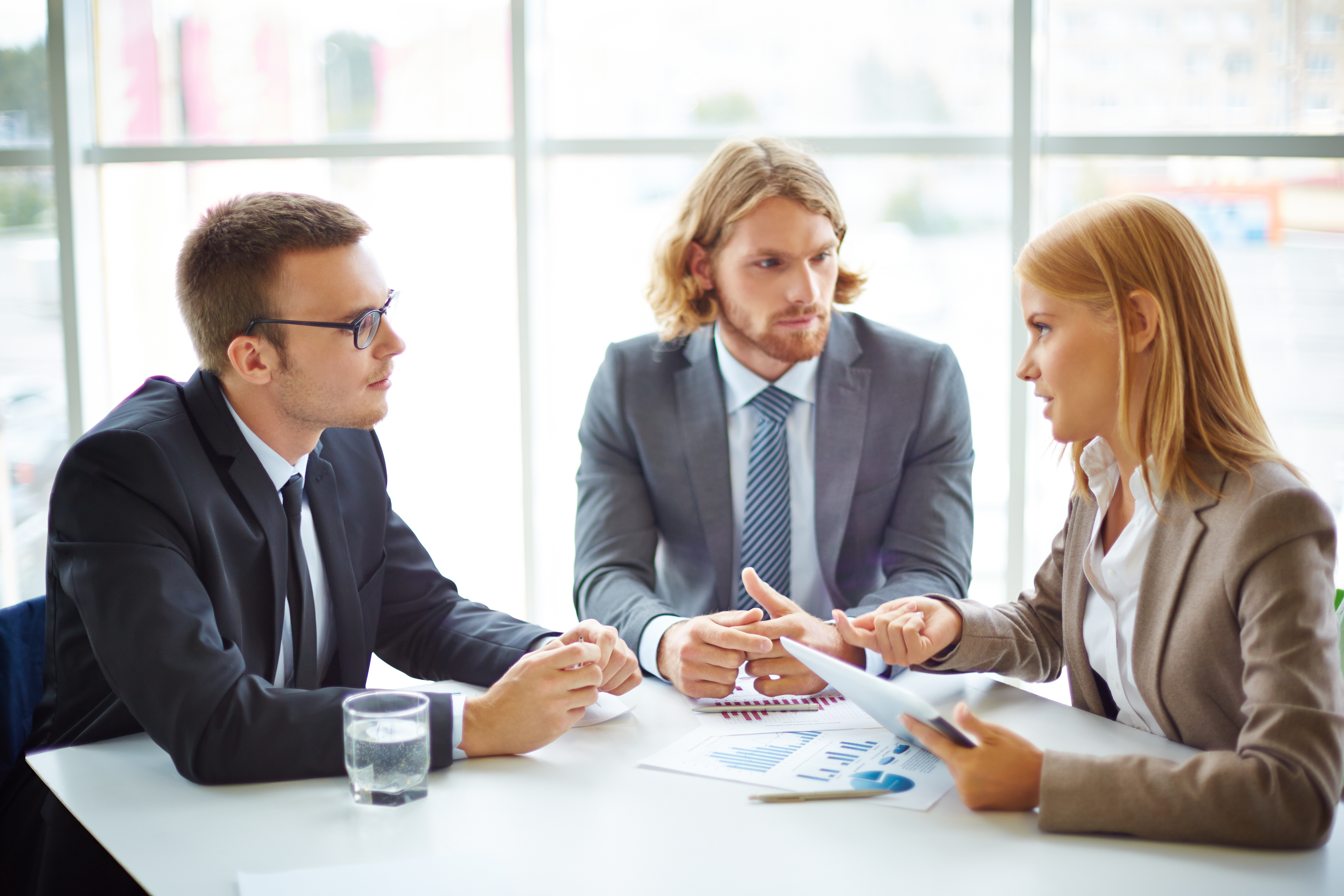 Two serious businessmen listening to their colleague at meeting in office